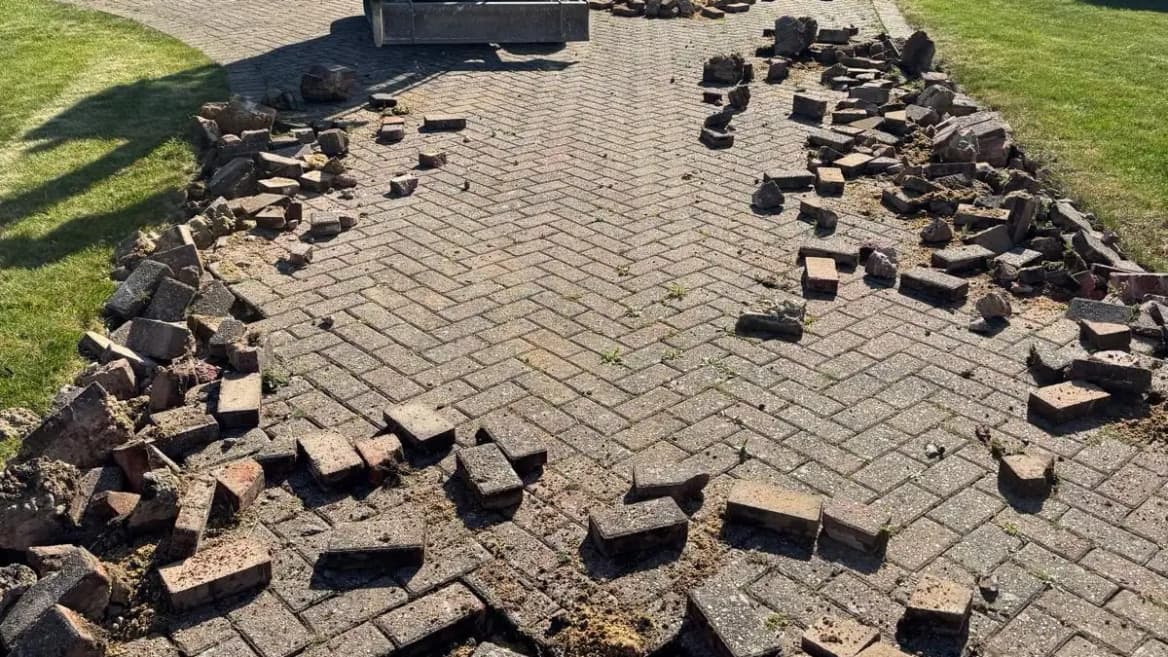 A worn block-paved driveway being lifted out for repair, the old blocks stacked ready to clear.