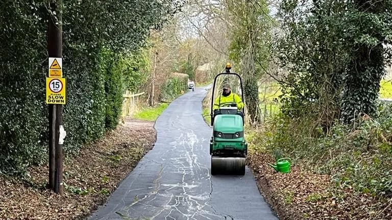 A private estate lane being resurfaced, fresh tarmac laid over the old surface and rolled in, past a 15mph sign.