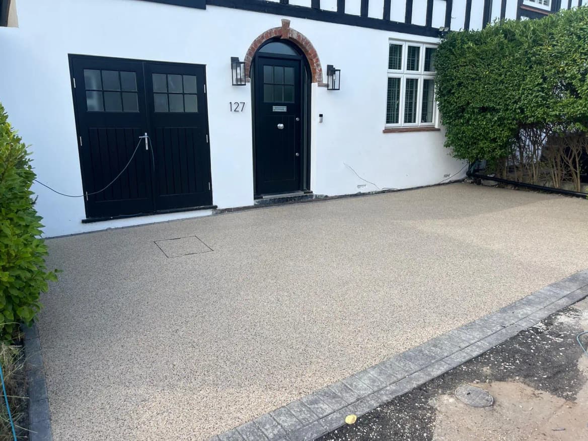 A finished gold resin-bound driveway with a charcoal block border in front of a period cottage.