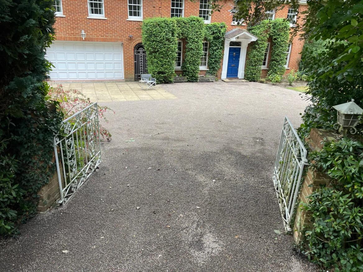 A freshly surface-dressed driveway with a fine stone finish, sweeping up to a large ivy-clad house.