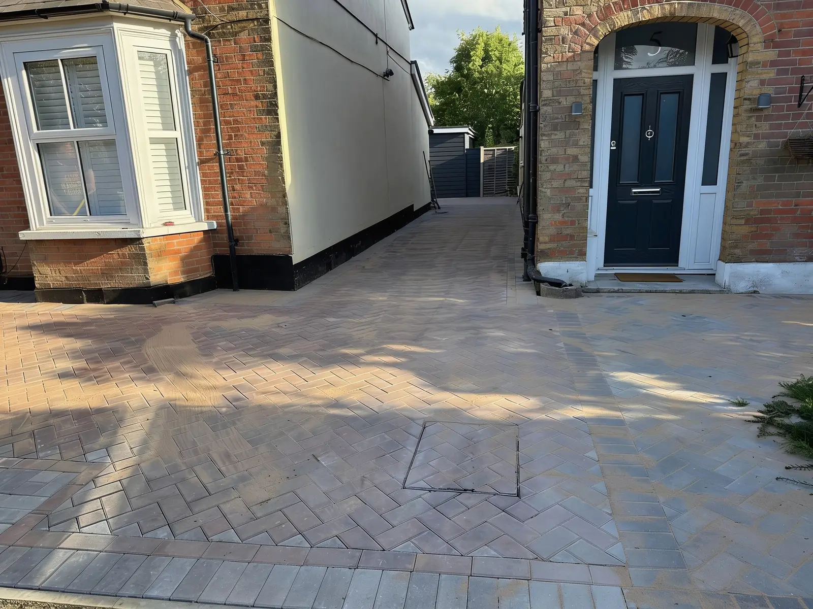 Finished brindle herringbone block paving forecourt with a charcoal soldier-course border at a period Surrey home